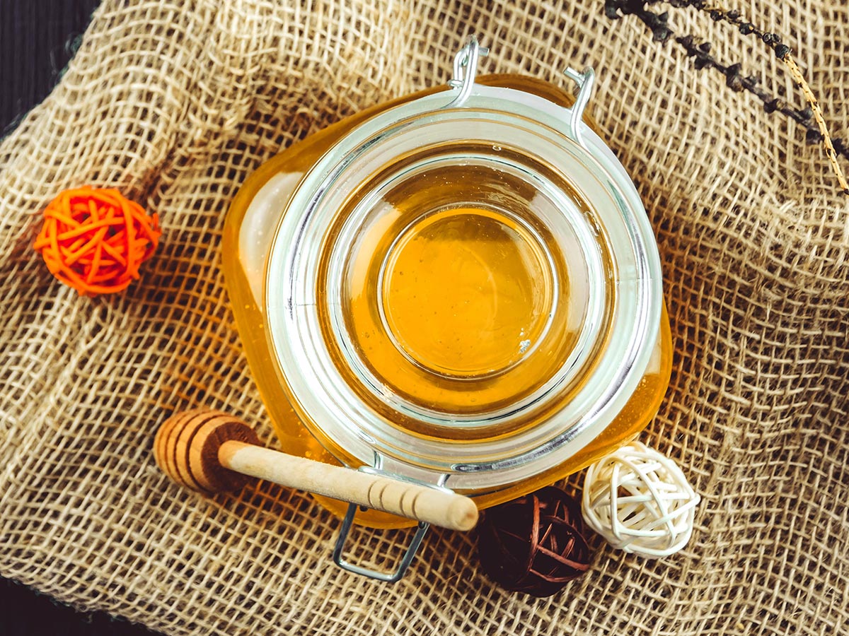 Jar of organic honey with a honey dipper on burlap